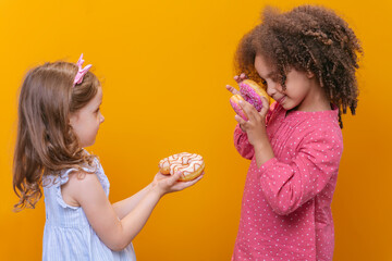 The girls are holding donuts in their hands on a yellow background. An African-American girl is playing with sweets.