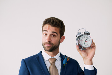 Wall Mural - Its time...Studio shot of a handsome young groom holding a clock against a gray background.