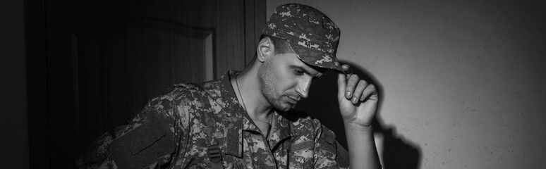 Poster - Black and white photo of upset soldier in uniform standing in hallway at home at night, banner.