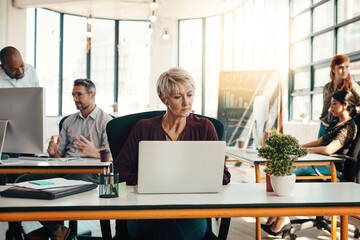 Aufkleber - On that get it done grind. a mature businesswoman using a laptop in a modern office with her colleagues in the background.