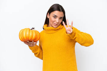 Wall Mural - Young caucasian woman holding a pumpkin isolated on white background happy and counting three with fingers