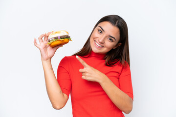 Wall Mural - Young caucasian woman holding a burger isolated on white background and pointing it