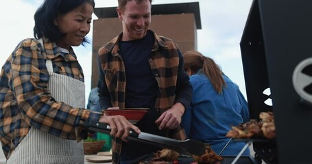 Wall Mural - Multi generational people doing barbecue during weekend day at home's rooftop preparing food - Multiracial friends having fun together - Asian woman cooking chili on bbq grill