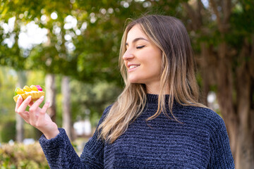 Wall Mural - Young pretty Romanian woman holding a tartlet at outdoors with happy expression