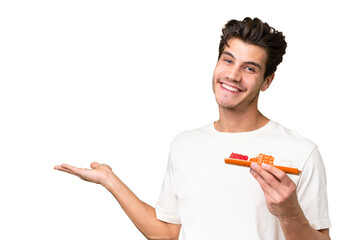 Wall Mural - Young caucasian man holding sashimi over isolated background extending hands to the side for inviting to come