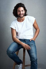 Wall Mural - Nothing more handsome than a genuine smile. Studio shot of a handsome young man sitting on a stool against a grey background.