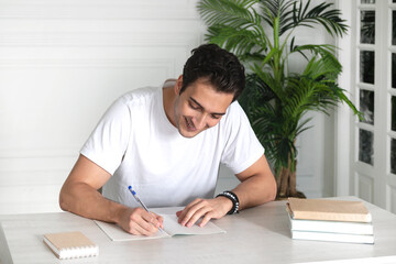 Portrait of young handsome student sitting at the desk with a stack of books. Education and preparation for exams concept