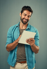 Poster - Hes happiest when hes connected. Studio shot of a handsome young man using a digital tablet against a grey background.