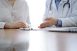 © rogerphoto - Doctor and patient discussing something while sitting near each other at the wooden desk in clinic. Medicine concept