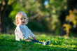 © Valua Vitaly - Portrait of a calm child with white curls sitting on the grass in the park on summer. A child is sitting on the grass in the park and looking at the camera. Cute quiet boy in white clothes on a walk