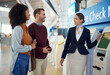 © Nina L/peopleimages.com - Woman, passenger assistant and couple at airport by self service check in station for information, help or FAQ. Portrait of happy female services agent helping travelers register or book air flight