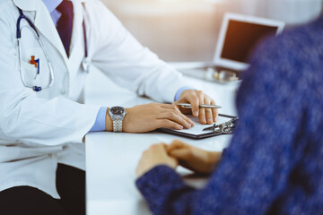 Wall Mural - Unknown doctors, two men and a woman, discuss medical exam resoults, while standing at sunny hospital office. Physicians using clipboards for filling up medication history records