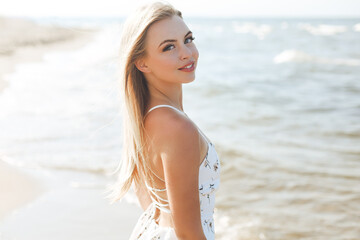 Happy blonde woman wearing sun glasses and relaxing on a wooden deck chair at the ocean beach