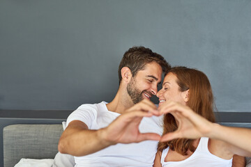 Wall Mural - The heart was made to love. a happy young couple relaxing in bed and making a heart gesture with their hands.