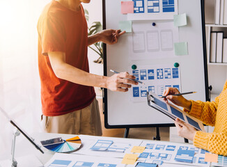 Close up ux developer and ui designer brainstorming about mobile app interface wireframe design on table with customer breif and color code at modern office.Creative digital development agency