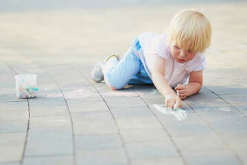 Little boy drawing with chalks on asphalt