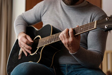 Playing The Guitar. Strumming Acoustic Guitar. Musician Plays Music. Man Fingers Holding Mediator. Man Hand Playing Guitar Neck In Dark Room. Unrecognizable Person Rehearsing, Fretboard Close-up