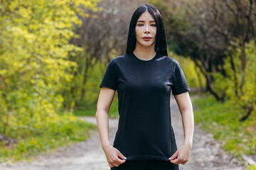 Wall Mural - Stylish brunette asian girl wearing black t-shirt posing against nature