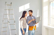 © Studio Romantic - Repairman with laptop talking to young woman. Worker with tool belt standing in room with step ladder, holding modern laptop computer and discussing repairs inside the house with young woman homeowner