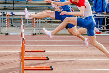 Wall Mural - three male runners attack hurdle running 100 meters race in summer athletics championships