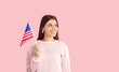 Cute smiling female american citizen with usa national flag isolated on pink background. Happy young woman celebrates America's Independence Day and with flag in hand smiling looks away at copy space.