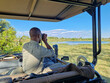 Ein Guide am Steuer eines Safari – Jeep beobachtet durch sein Fernglas die Savanne von Botswana im Okavango Delta