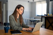 © Dorde - Serious dedicated businesswoman using laptop sitting at the table in a home office, looking at device screen, communicating online, writing emails, distantly working or studying on computer at home.