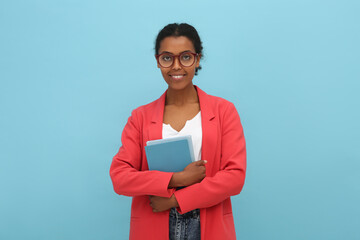 Canvas Print - Smiling African American intern with books on light blue background