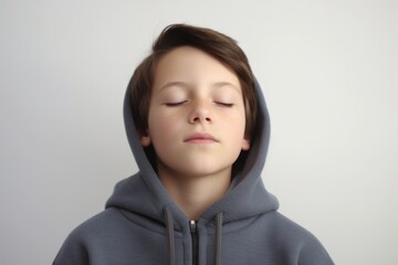 A boy in a gray hoodie with closed eyes on a gray background