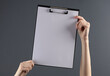 © splitov27 - Female hands holding a clipboard with an empty white sheet on a dark background