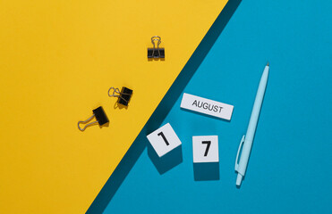 White cube calendar with the date august 17 with stationery, or office accessories on a blue yellow background. Deadline, business concept