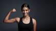 © Angelo/peopleimages.com - Portrait, smile and woman flexing bicep in studio isolated on a black background mockup space. Strong, happy and female athlete with muscle, arm strength and bodybuilder ready for fitness workout.
