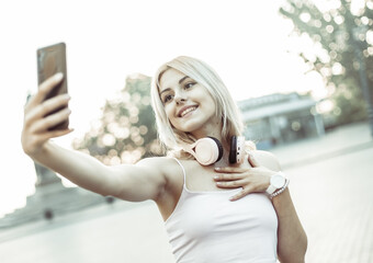 Wall Mural - Young smiling blonde woman makes selfie on the phone in the city