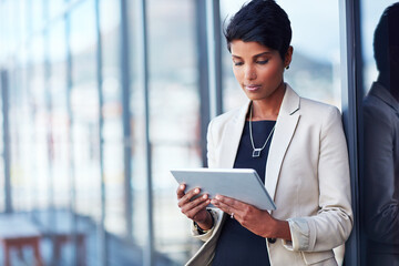 Tablet, mockup and corporate with a business woman leaning against a glass wall or window at the office. Technology, research and space with a young professional female employee working online