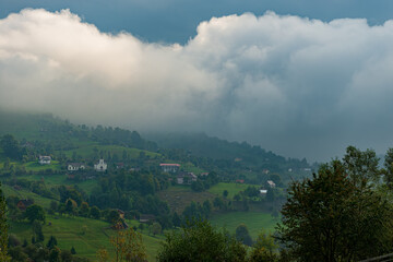 Wall Mural - Rural idyllic landscape of the small villages in the Rucar-Bran mountain area, Brasov, Romania, scattered on the wooded hills, with the Bucegi mountains in the background, in wonderful springtime day