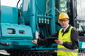 Poster - Engineer in a helmet with a digital tablet stands next to construction excavators