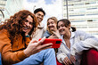 Group of young gen z friends sitting together in the city using cell phone app to share funny content