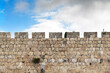 Background with fragment of the upper part of the fortress wall of Jerusalem Old City with the blue sky and clouds on the background