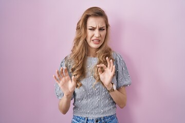 Sticker - Beautiful blonde woman standing over pink background disgusted expression, displeased and fearful doing disgust face because aversion reaction.