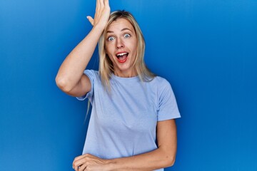 Sticker - Beautiful blonde woman wearing casual t shirt over blue background surprised with hand on head for mistake, remember error. forgot, bad memory concept.