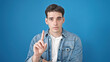 Young hispanic man standing with serious expression saying no with finger over isolated blue background