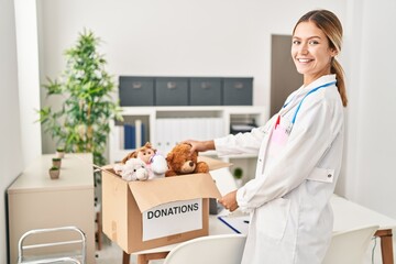 Wall Mural - Young hispanic woman wearing doctor uniform donate toys at clinic