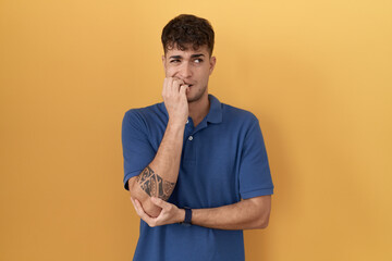 Sticker - Young hispanic man standing over yellow background looking stressed and nervous with hands on mouth biting nails. anxiety problem.