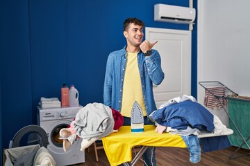 Sticker - Young hispanic man ironing clothes at home pointing thumb up to the side smiling happy with open mouth