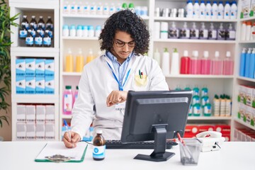 Poster - Hispanic man with curly hair working at pharmacy drugstore checking the time on wrist watch, relaxed and confident