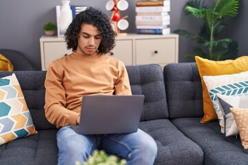 Sticker - Young latin man using laptop sitting on sofa at home