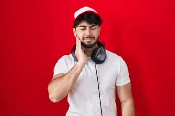 Canvas Print - Hispanic man with beard wearing gamer hat and headphones touching mouth with hand with painful expression because of toothache or dental illness on teeth. dentist