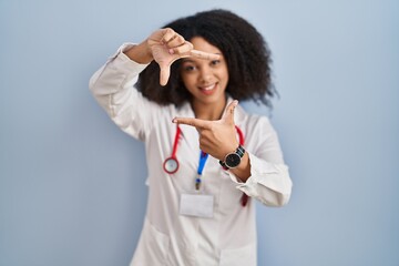 Wall Mural - Young african american woman wearing doctor uniform and stethoscope smiling making frame with hands and fingers with happy face. creativity and photography concept.