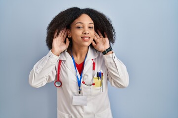 Wall Mural - Young african american woman wearing doctor uniform and stethoscope trying to hear both hands on ear gesture, curious for gossip. hearing problem, deaf
