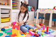 © Krakenimages.com - Adorable hispanic girl playing with construction blocks sitting on floor at kindergarten